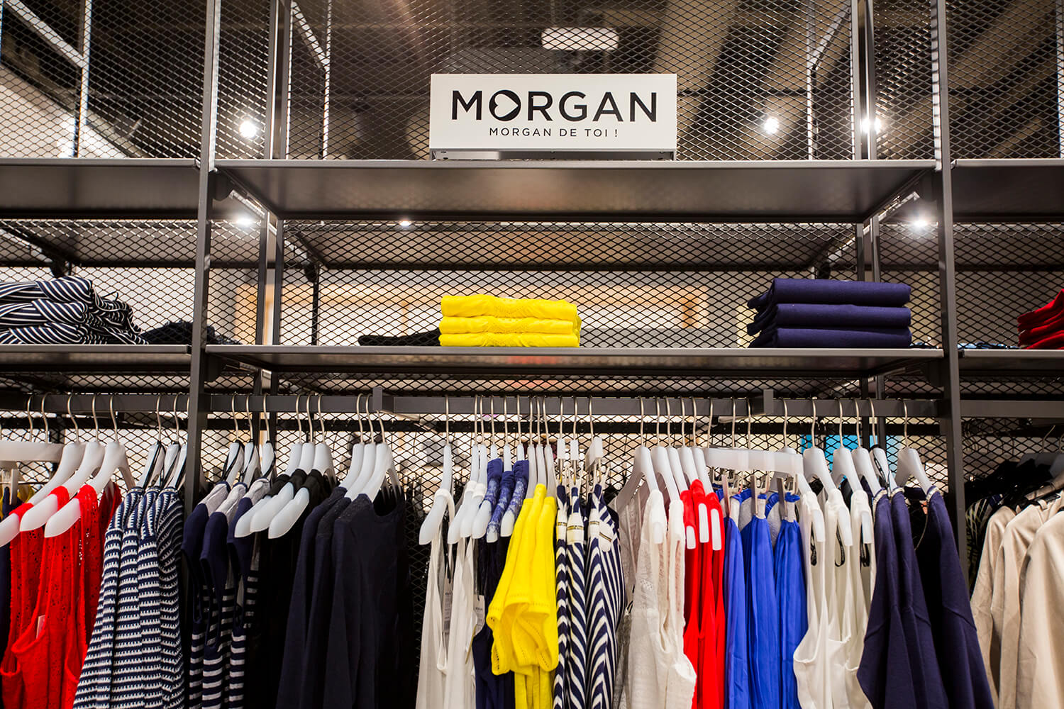 Oblačila znamke Morgan na temno sivih kovinskih regalih s kovinsko mrežo na zadnji strani v trgovini Sportina Outlet
