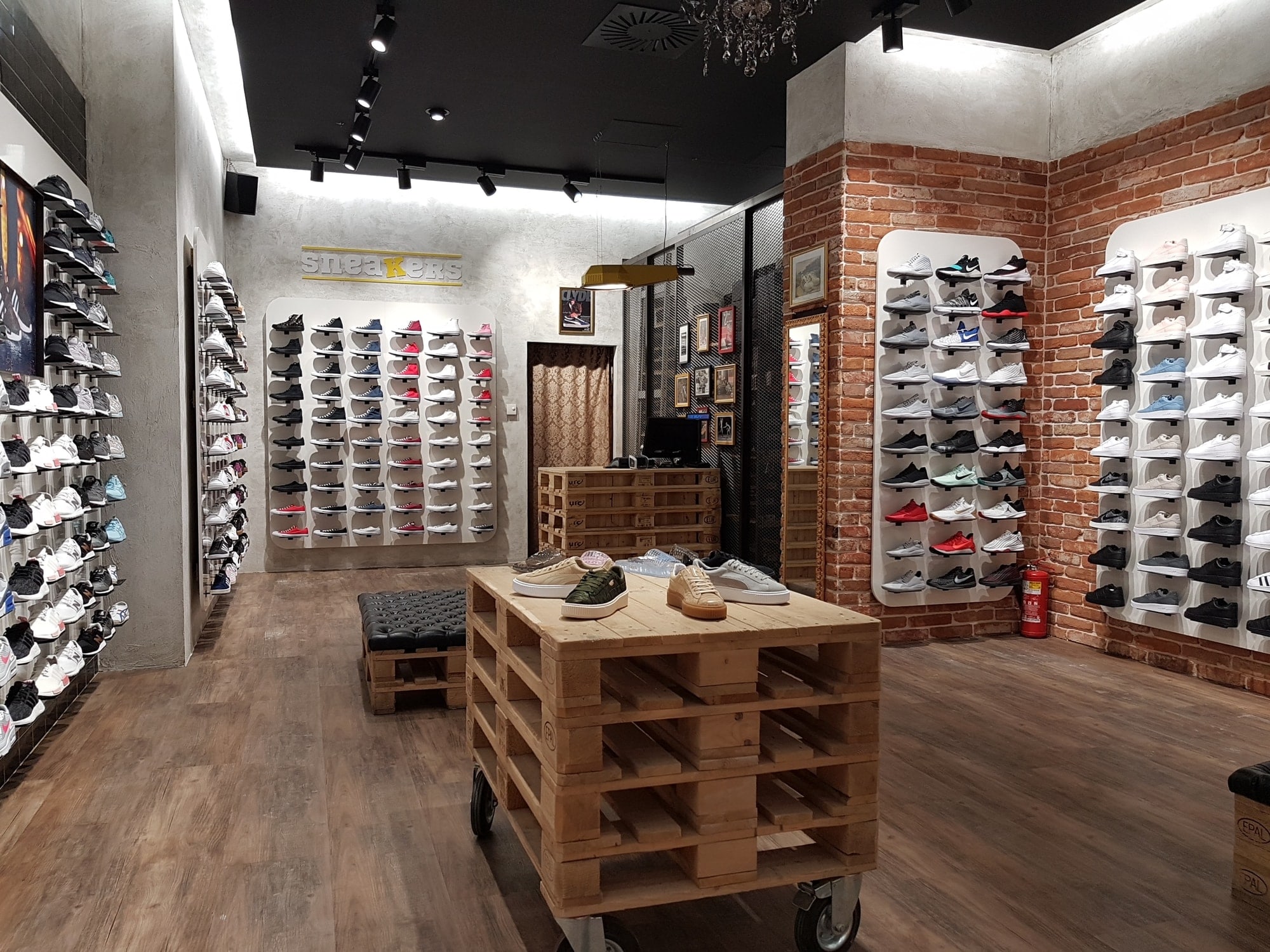 Opečnata stena s športnimi copati in lesene palete v ospredju v trgovini Sneakers